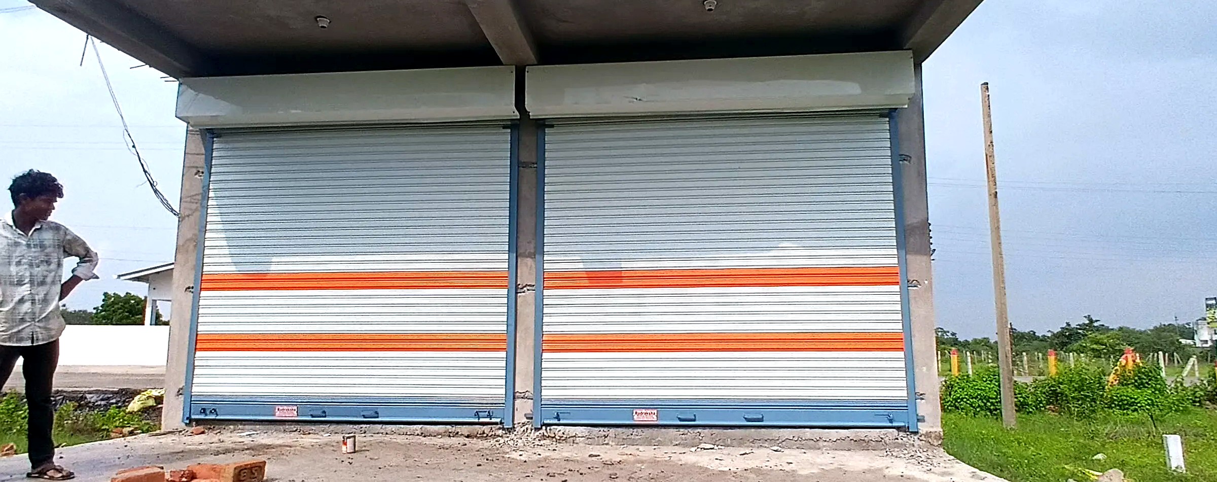 Twin white rolling shutters with orange stripe, outdoor installation, Nagpur